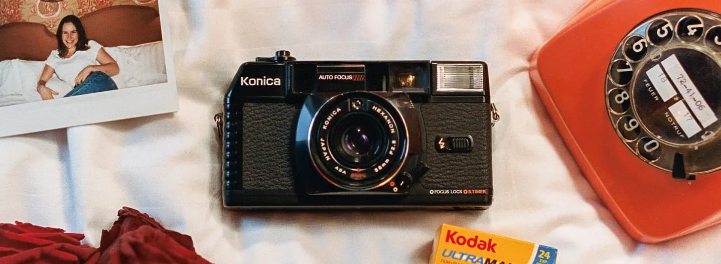 A film camera, photographs, flowers and an orange telephone arranged on fabric.