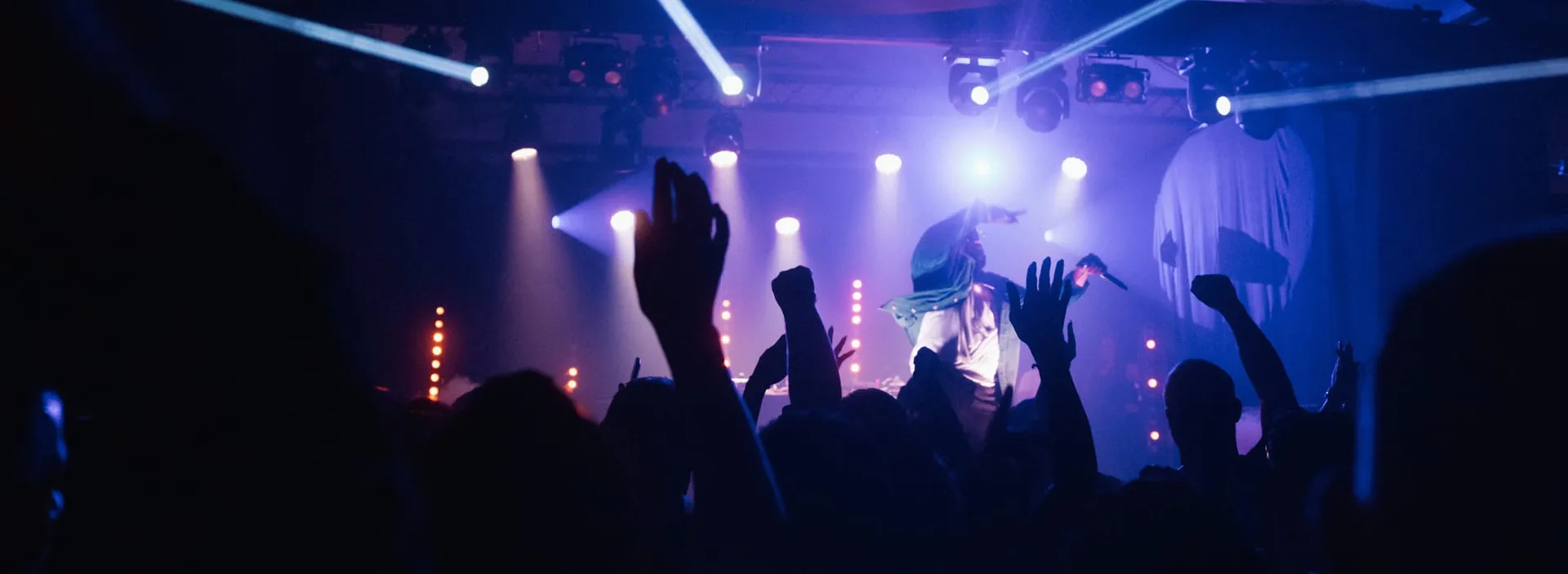 A concert crowd raising their hands beneath blue stage lights.