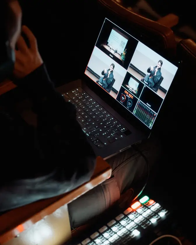 An operator monitors several camera angles on a laptop beside a video switcher.