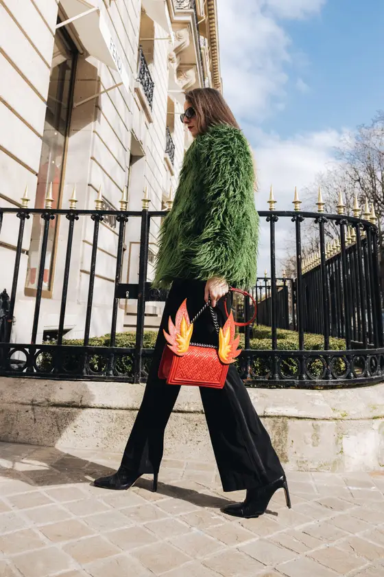 A woman carrying a handbag walks beside a building in a green jacket.