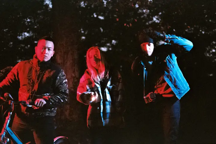 Three people photographed outdoors at night under red and blue light.