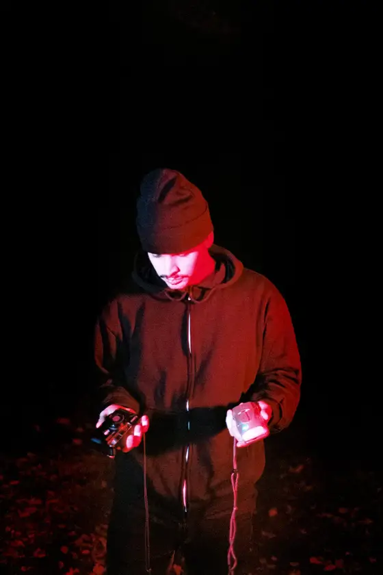 A person in a dark jacket photographed at night under red light.