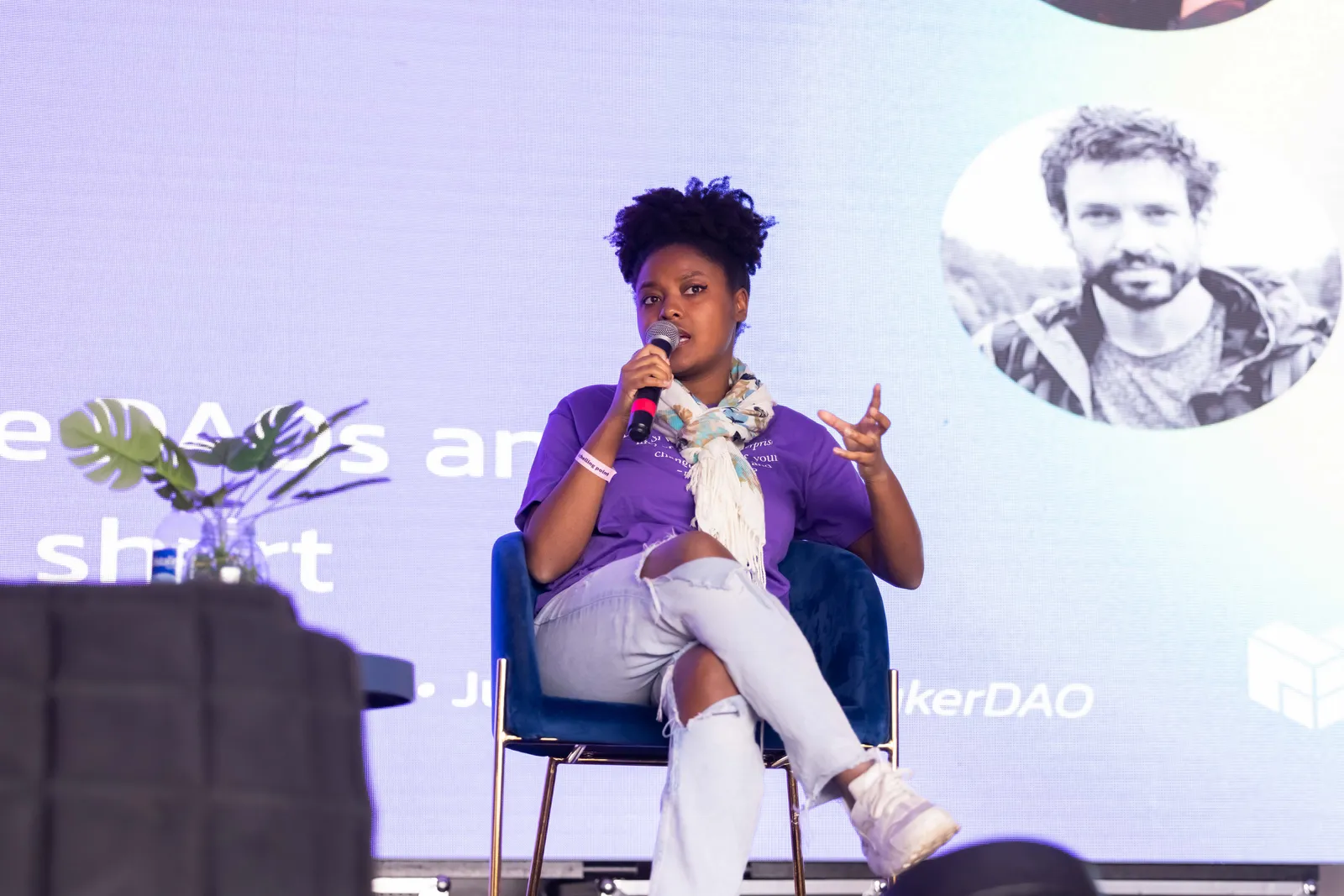 A panelist speaking, with a presentation slide visible on the screen behind her.