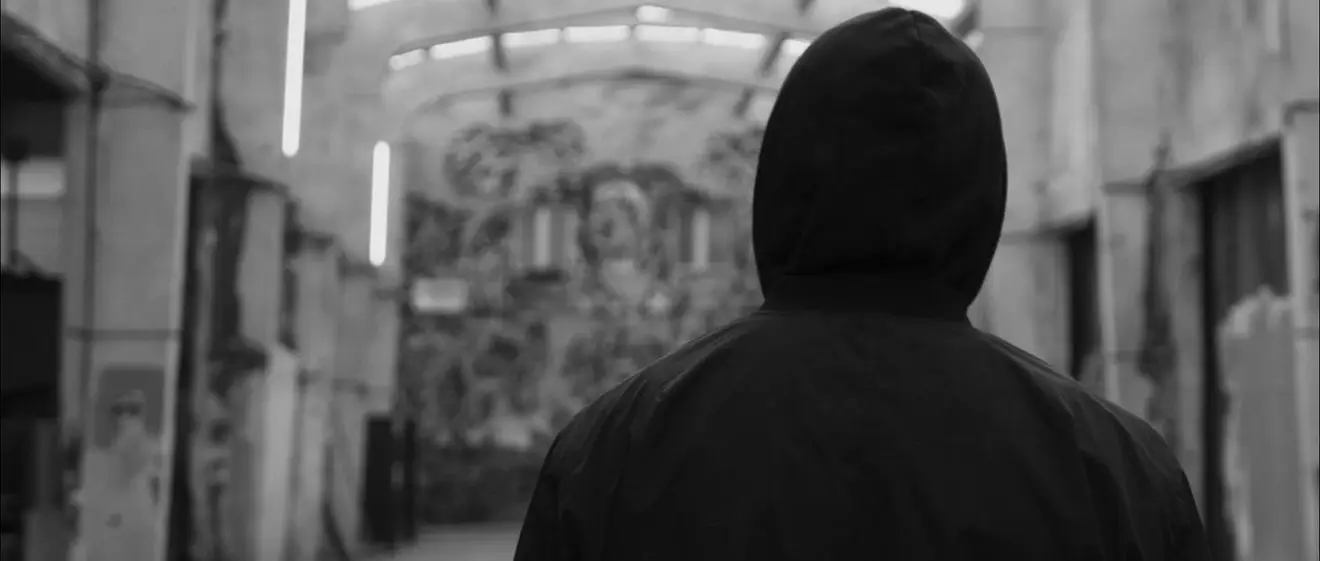 Une silhouette encapuchonnée devant un mur couvert de fresques
